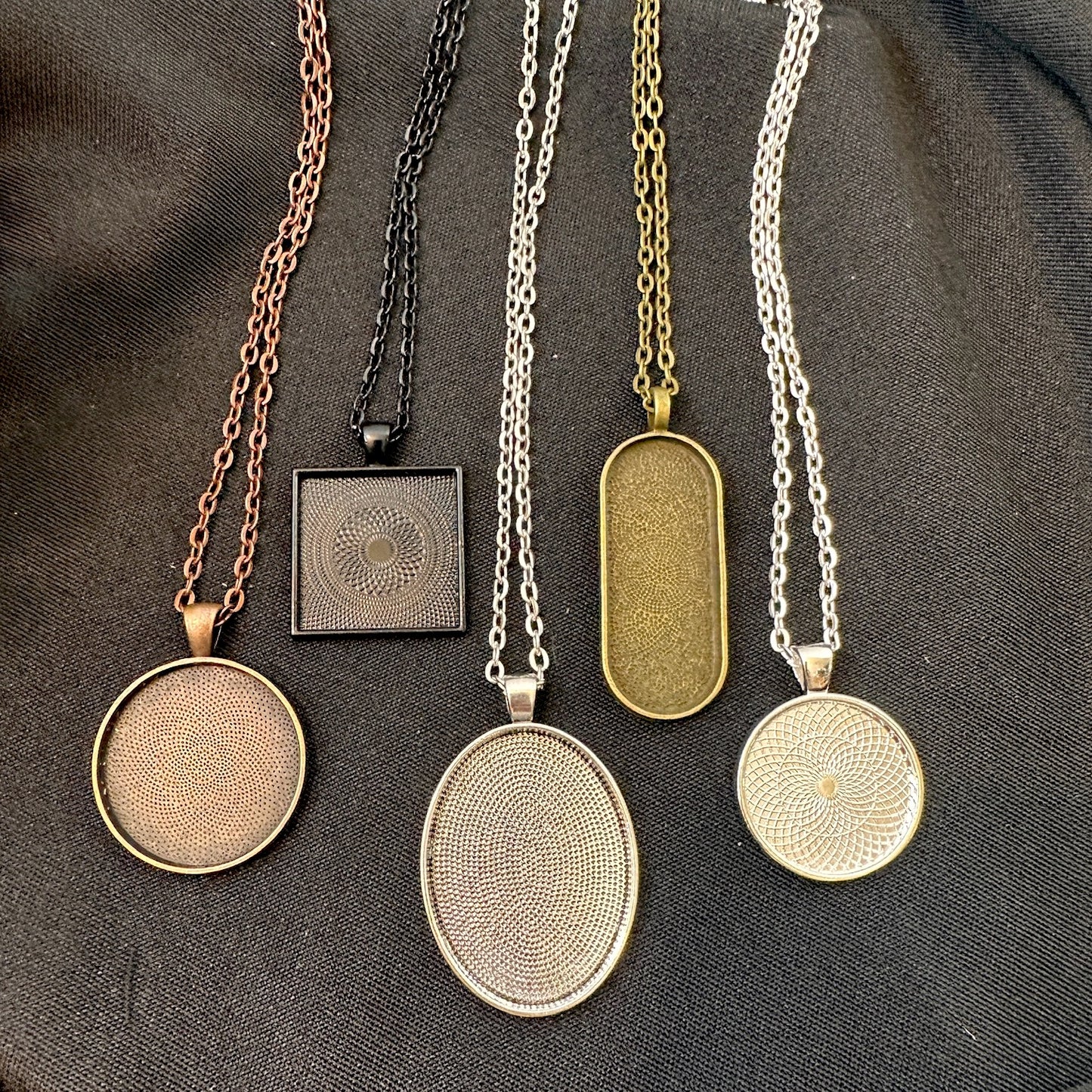 Set of five necklaces with various pendant designs on a dark fabric background