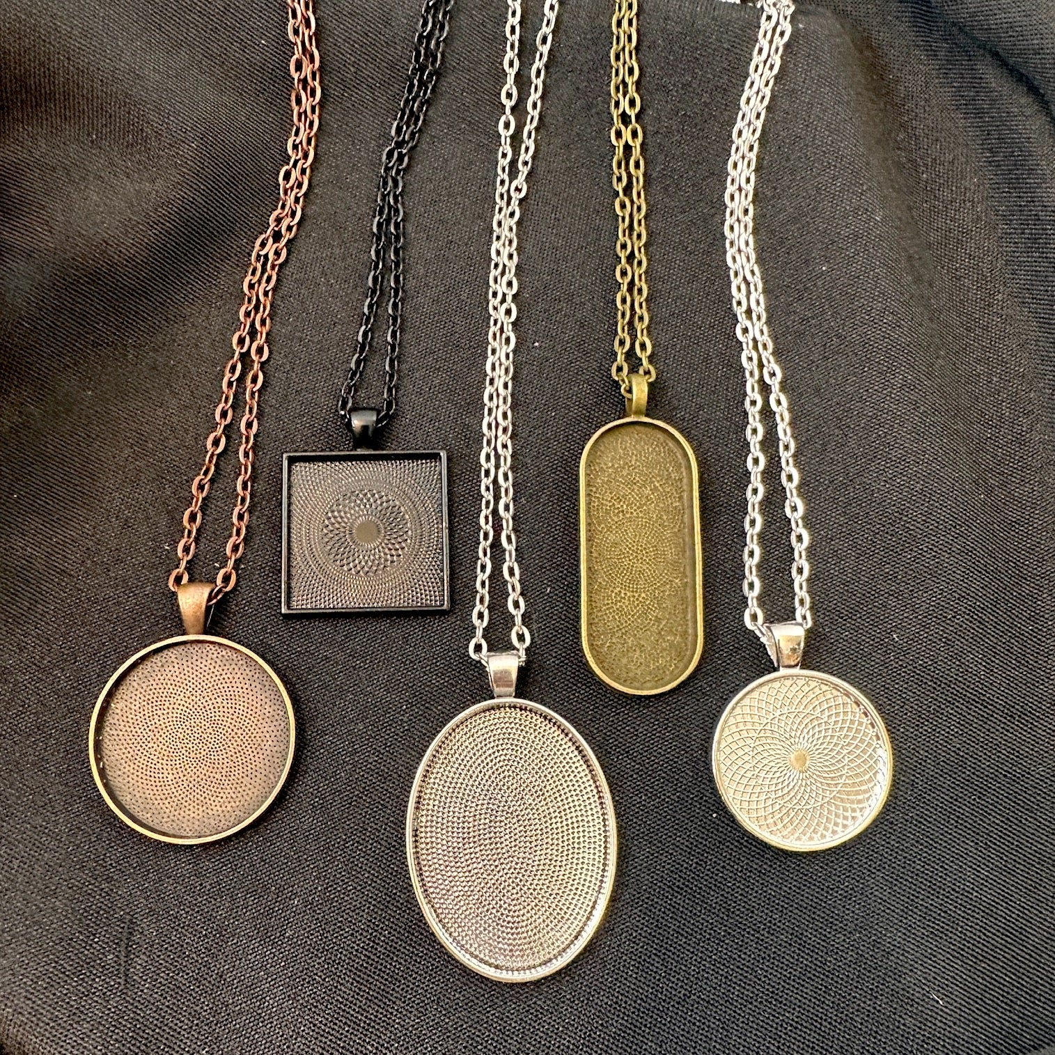 Set of five necklaces with various pendant designs on a dark fabric background